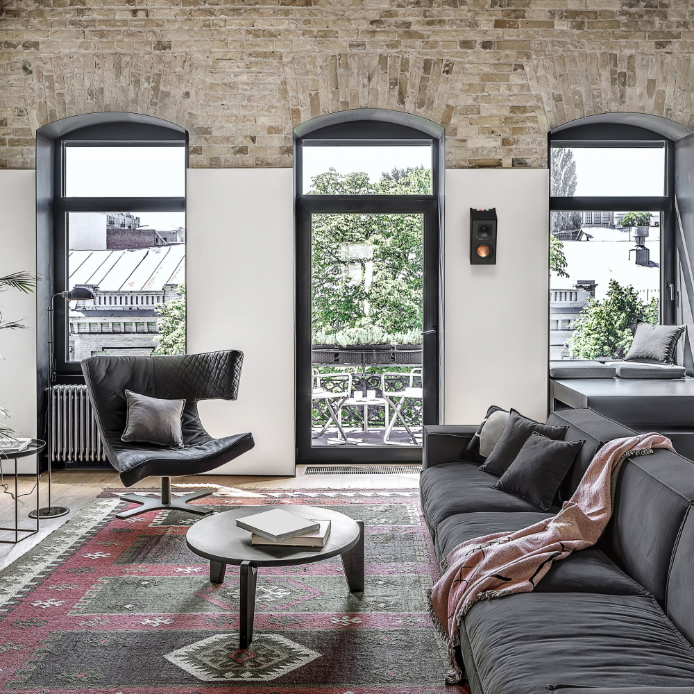 Modernt vardagsrum med en soffa, fåtölj och växt. Klipsch-högtalare på väggen.