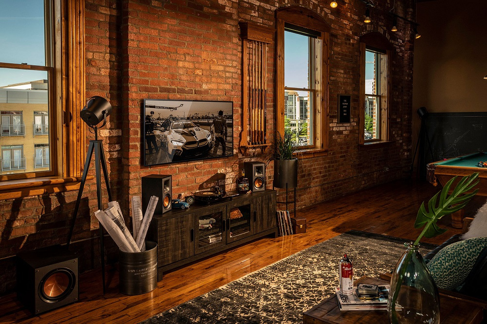 Inredning med tegelvägg, TV, högtalare, bord och golvlampa i ett modernt rum.