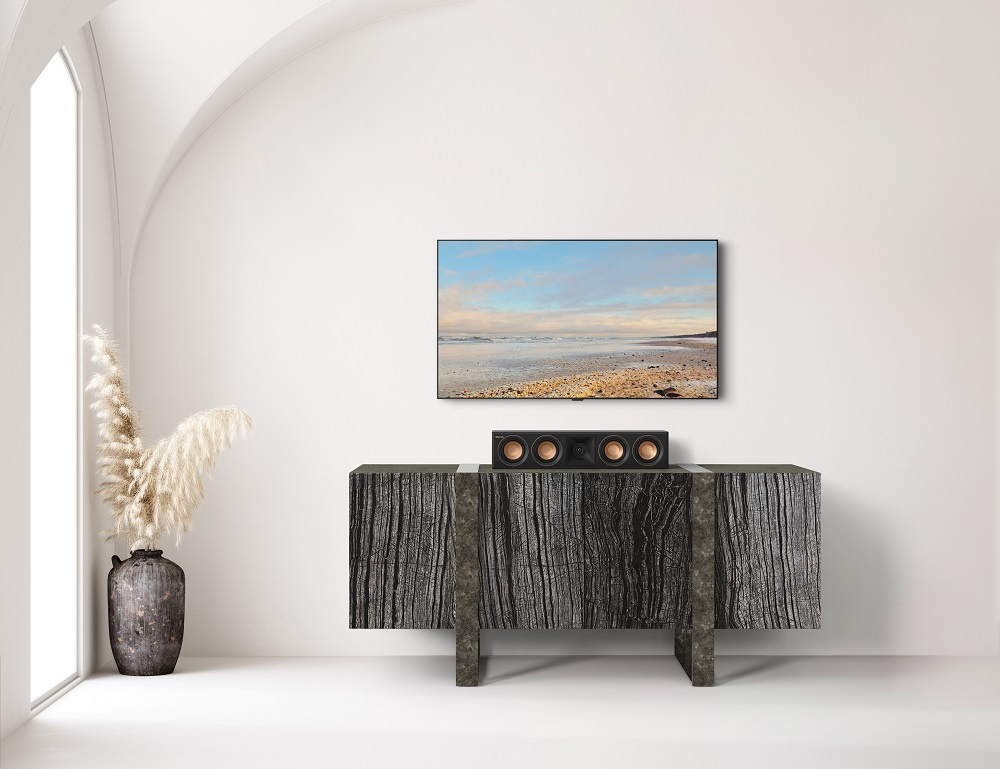 En svart centerhögtalare placerad på en modern bänk under en TV.