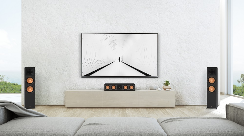 Svarta golvhögtalare med träfinish bredvid en TV i modern inredning.