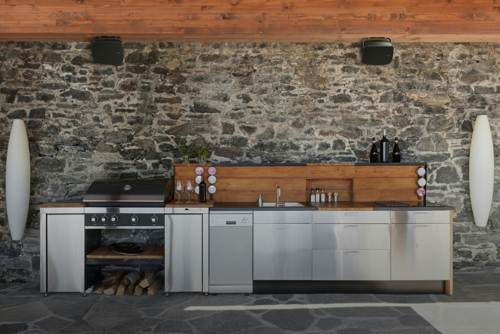 Utomhuskök med grå stenvägg och svart högtalarpar ovanför.