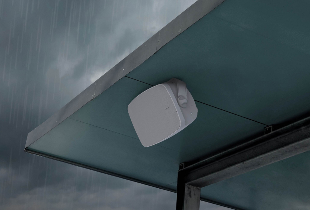 Två vita utomhushögtalare monterade under ett tak med mörka moln i bakgrunden.