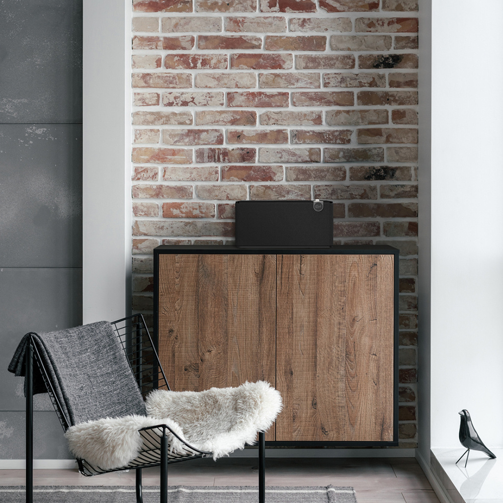 En svart högtalare på en träbänk framför en tegelvägg.