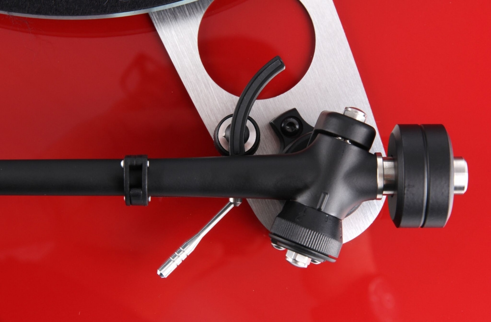 En skivspelare med arm och pick-up på en röd yta.