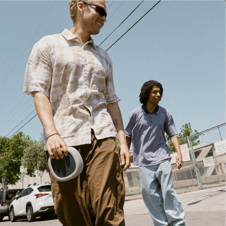 Två män går på gatan, en håller en rund Bluetooth-högtalare. Soligt väder.