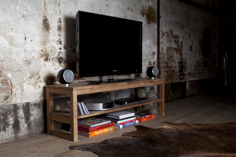 Svart klothögtalare på ett soffbord framför en TV i en rustik miljö.