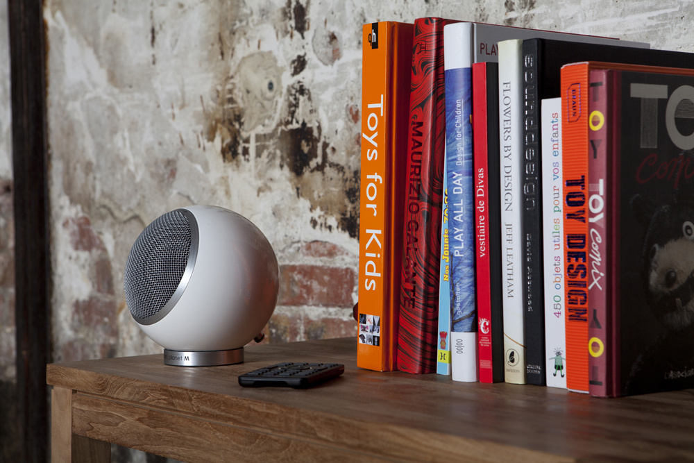 En vit klothögtalare bredvid en bokhylla med böcker.