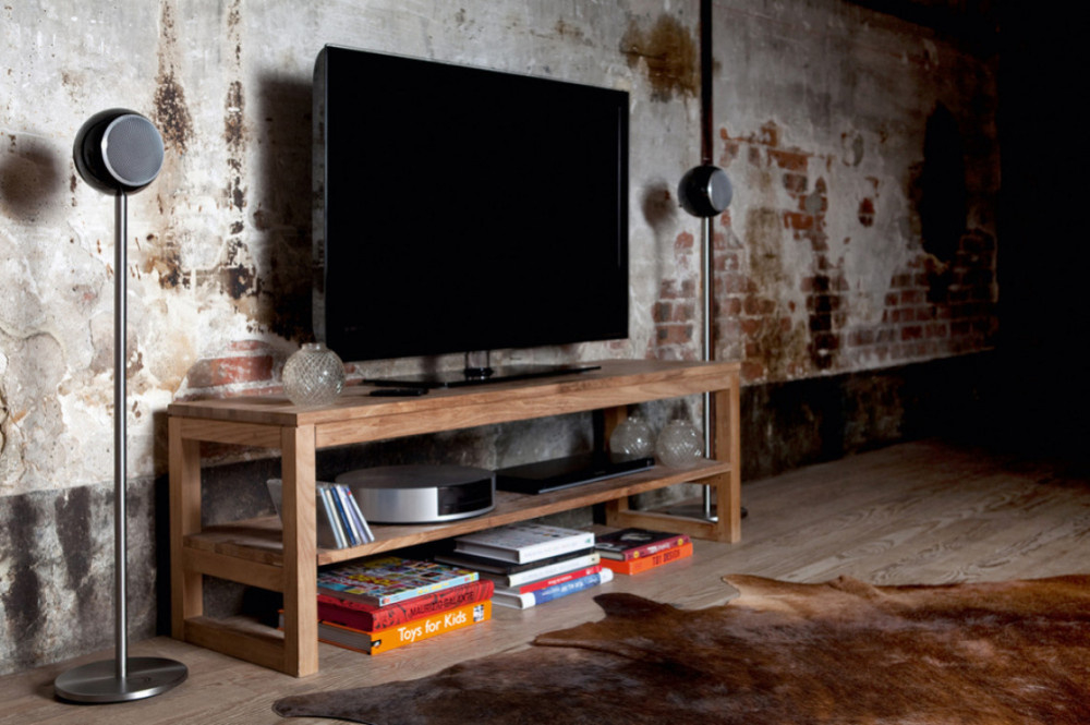 Tv-ställ med högtalare, böcker och dekorativa föremål i en rustik miljö.