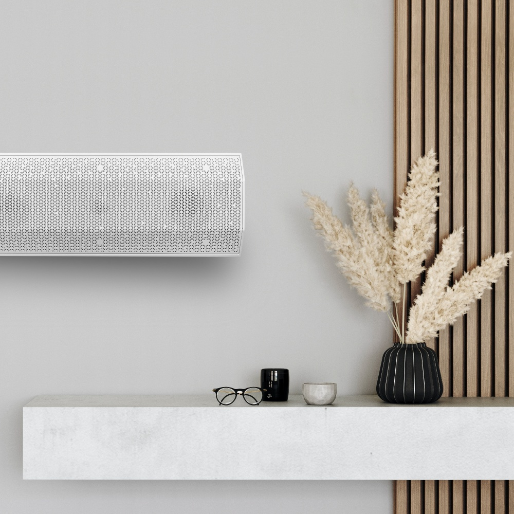 En vit passiv högtalare med stilrena detaljer på en hylla, omgiven av dekorationer.