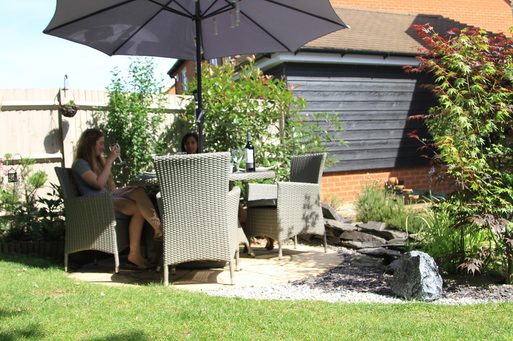 Trädgårdsmöbler under parasoll, två personer njuter av en dryck.