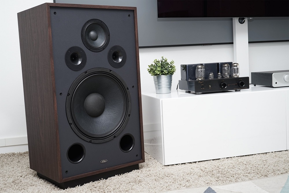 En stor golvhögtalare i valnöt med svarta detaljer och en ljudanläggning bredvid.