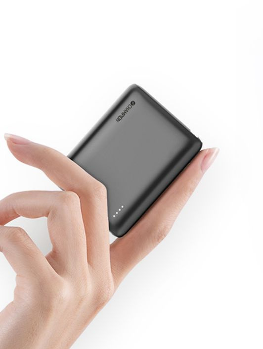 En hand håller en kompakt, mörk powerbank med tre indikatorlampor.