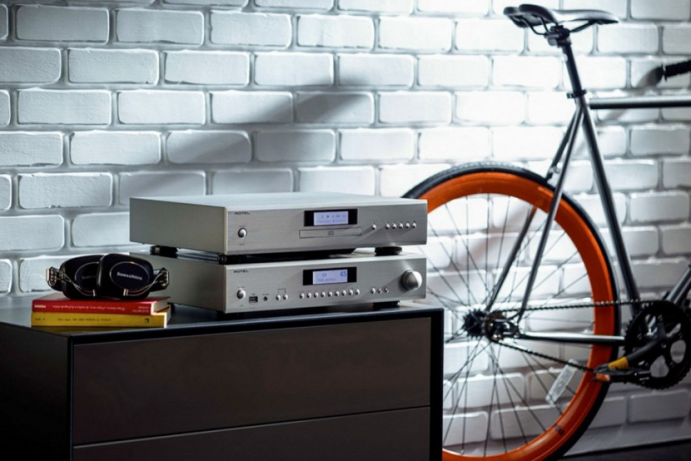 Silverfärgad CD-spelare ovanpå svart möbel med en cykel i bakgrunden.