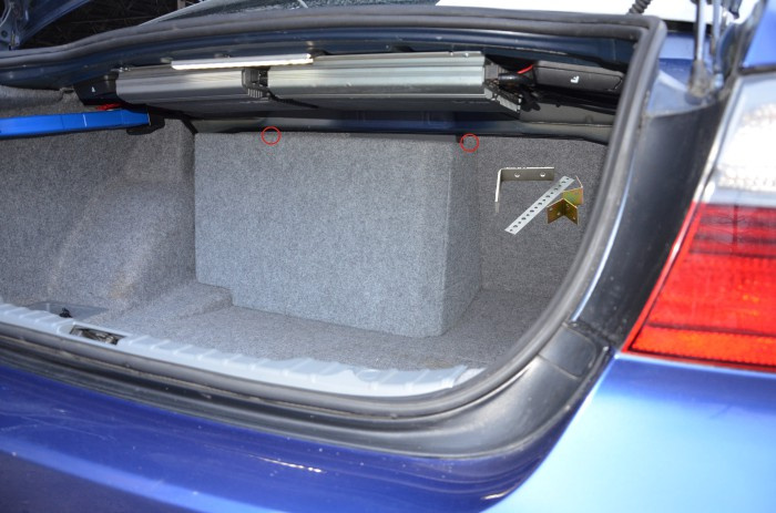 Bilden visar en bils bagageutrymme med tom baslåda och installationstillbehör.