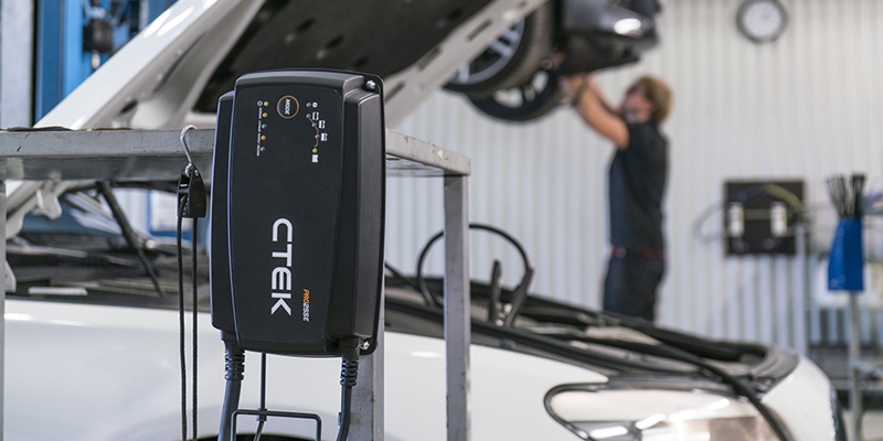 Laddare för bilbatteri med en mekaniker i bakgrunden.