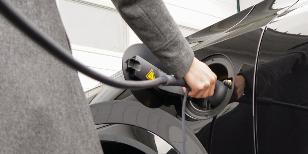 En person ansluter en laddkabel till en elbil.