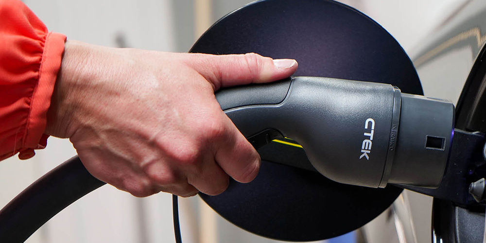 En hand kopplar en CTEK laddkabel till en elbil.