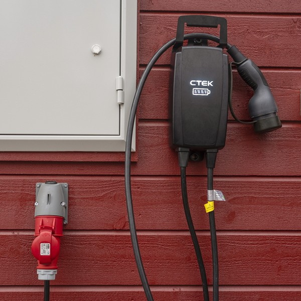 Väggfäste med laddare och kabel för elbil, monterat på en röd vägg.