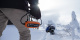 CTEK MXS 5.0 Polar Edition, batteriladdare anpassad för kalla klimat Person håller en orange batteriladdare i snöigt landskap med en snöskoter i bakgrunden.