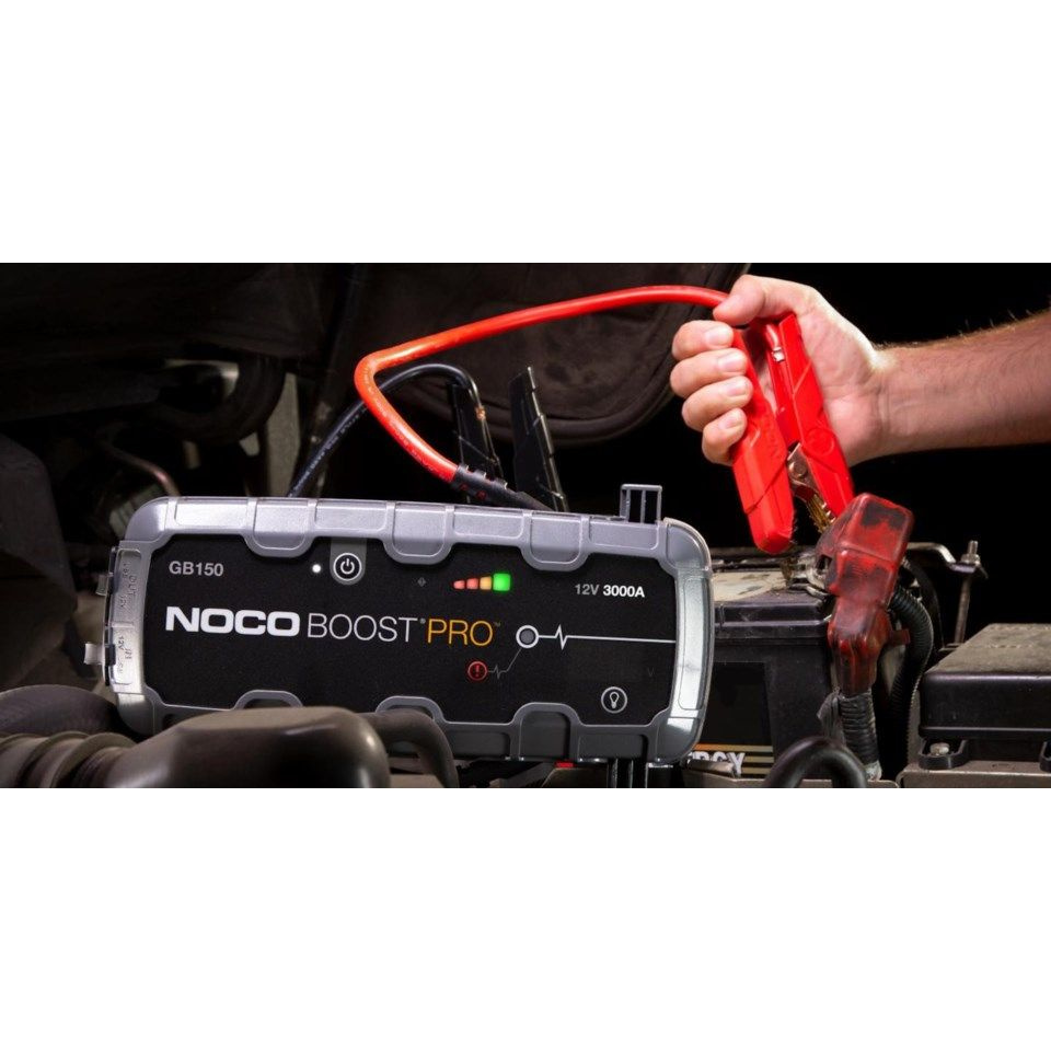 En hand kopplar en NOCO Boost Pro GB150 startbooster till en bilmotor.