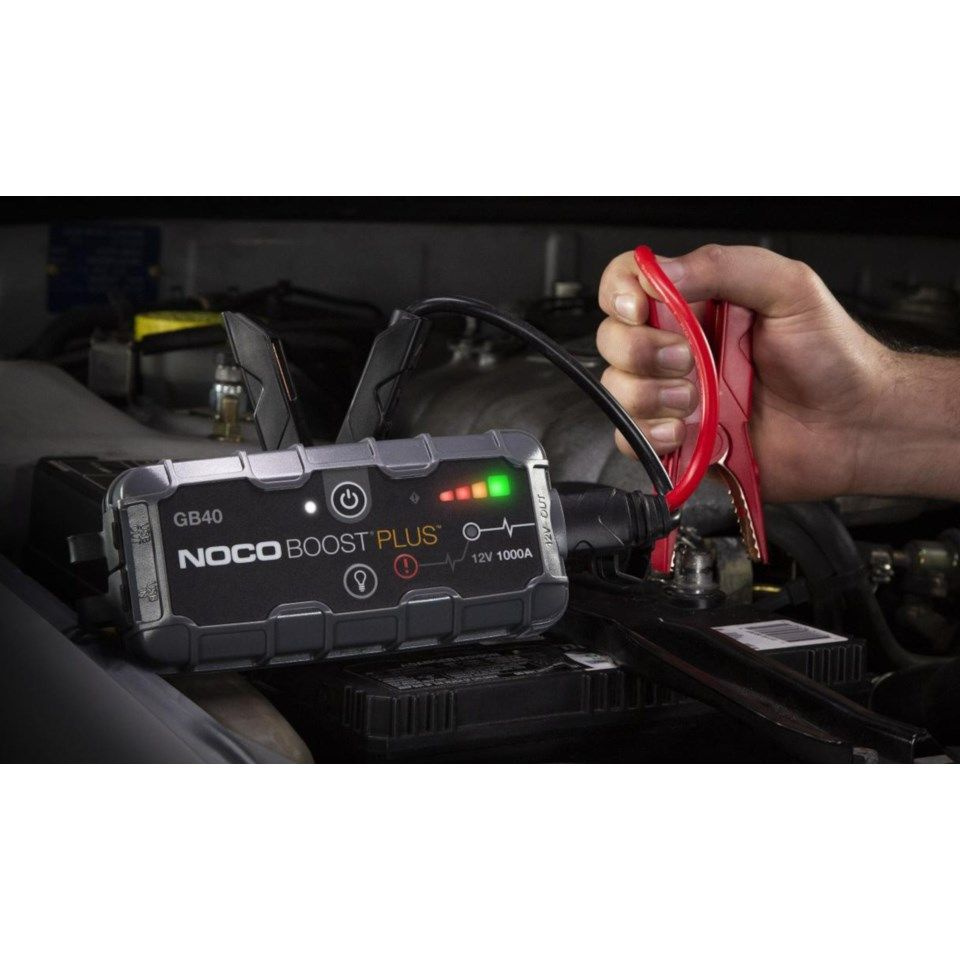 En hand kopplar en startbooster till en bilbatteri. Produktens indikatorer lyser.