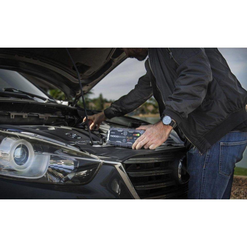 En person använder en NOCO Boost Plus GB40 startbooster på en bilmotor.