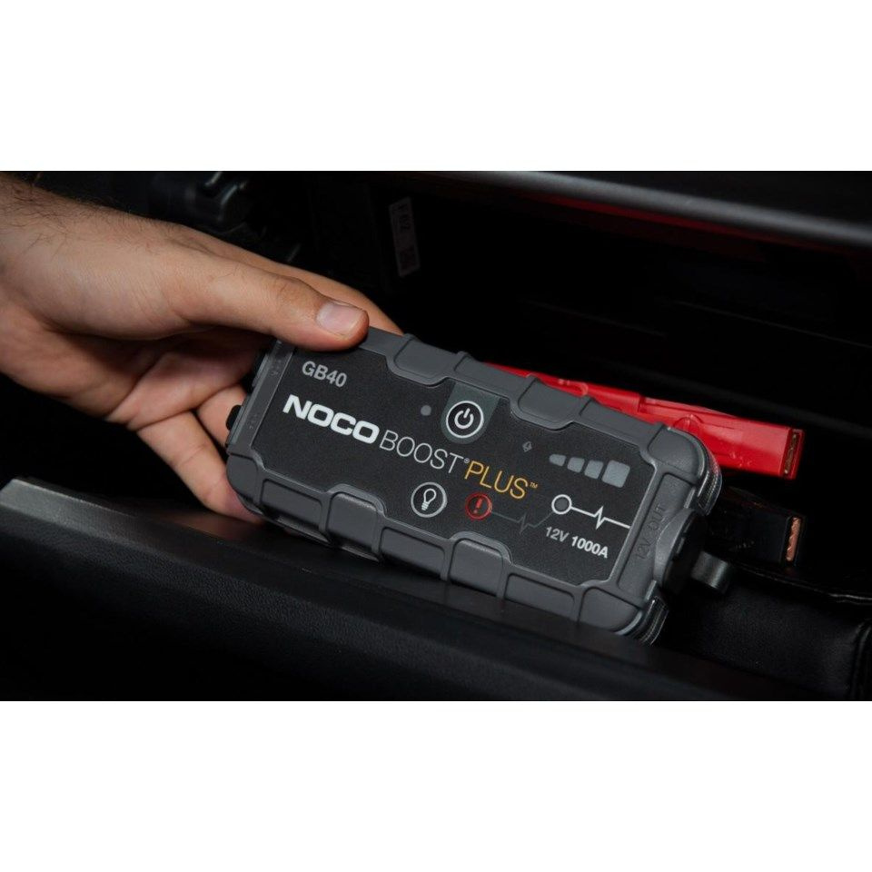 En hand håller en NOCO Boost Plus GB40 startbooster i en bil.