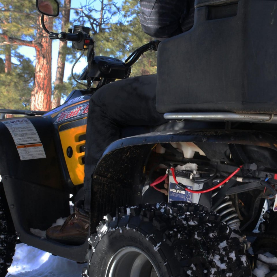 En person sitter på en fyrhjuling i snöig terräng.