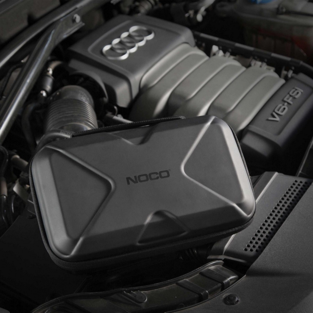 Svart förvaringsväska med NOCO-logotyp ligger på bilens motor.