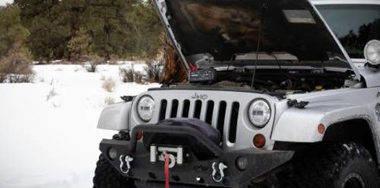 En silverfärgad jeep med motorhuven öppen i snöigt landskap.