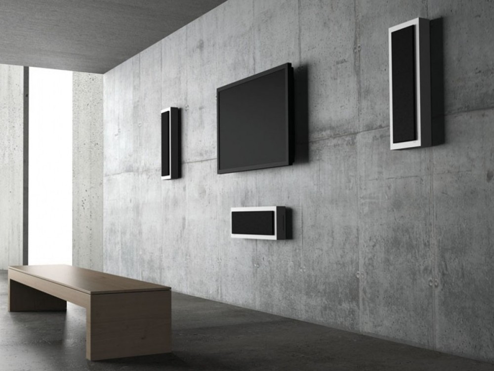 Högtalare i matt vitt monterade på vägg, minimalistisk inredning med tv och bänk.