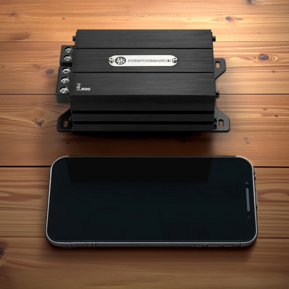 En kompakt monoblock förstärkare och en mobiltelefon på en träyta.