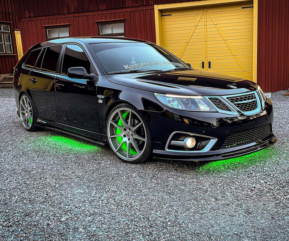 En svart bil med grönt underbelysning parkeras framför ett rödbrunt hus.