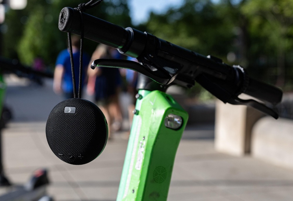 En svart, rund Bluetooth-högtalare hänger på en el-scooter.