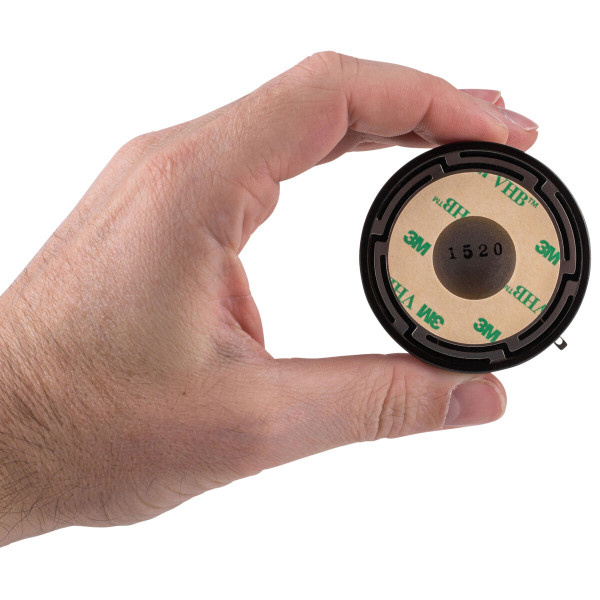 En hand håller i en rund exciter med 3M-tejp på baksidan.