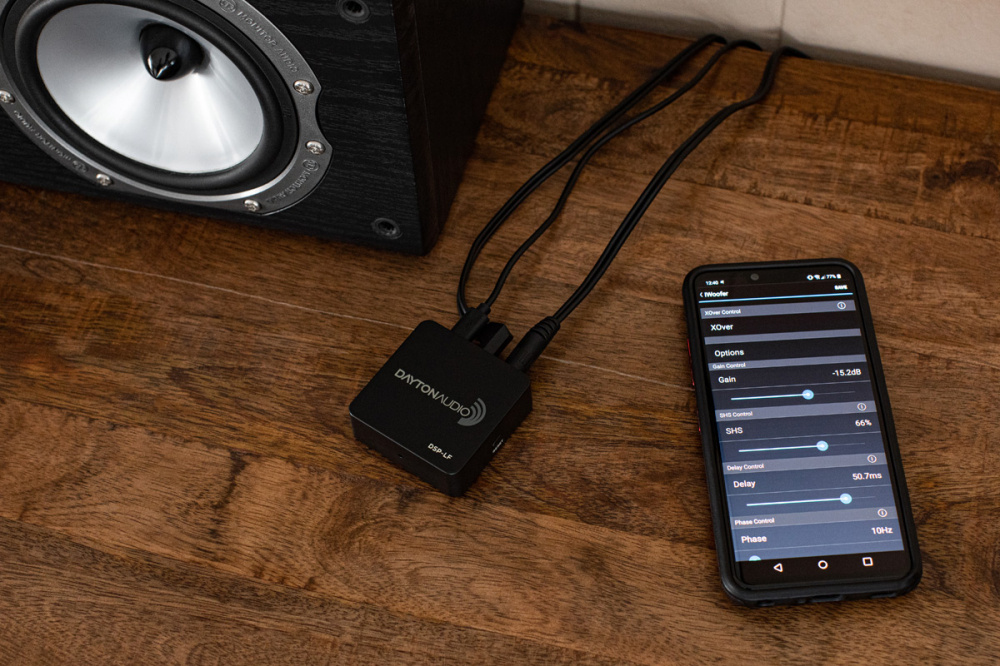 En svart DSP-enhet kopplad till en högtalare och en smartphone med EQ-inställningar.