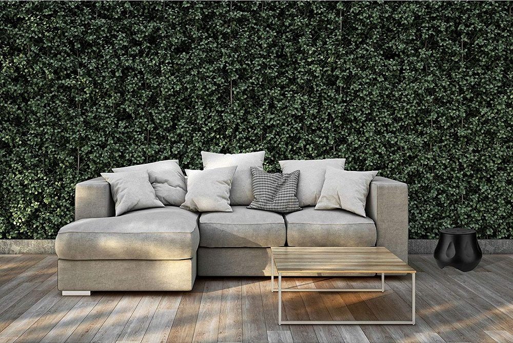Modern soffa med kuddar, soffbord och grön vägg av växtlighet.