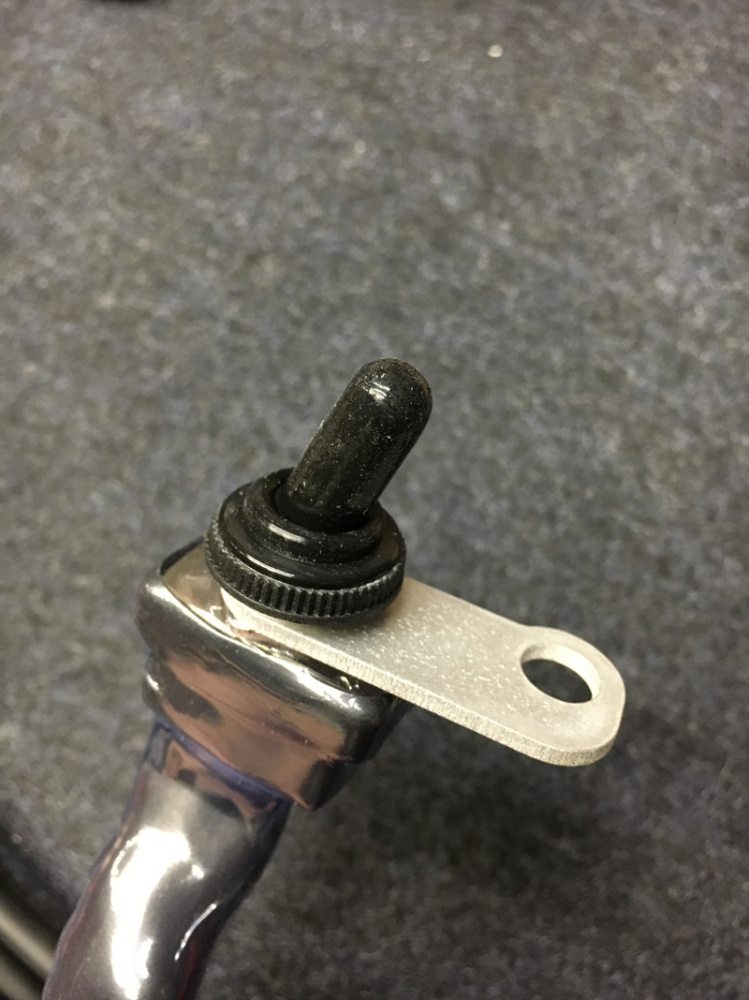 Fäste till strömbrytare, metall med svarta detaljer.