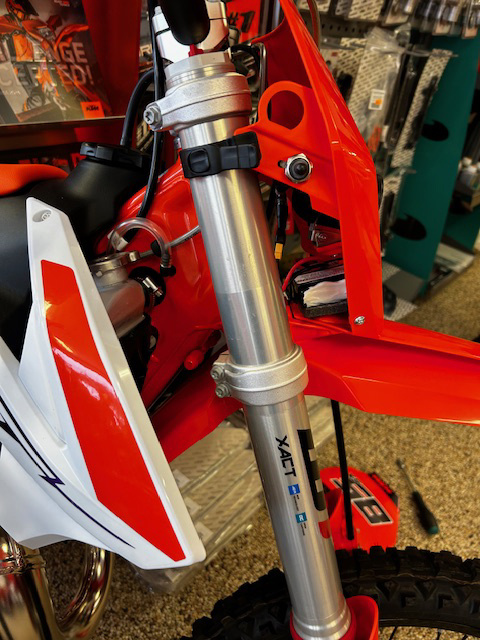 En del av en motorcykel med röd och vit kåpa och en metallisk stötdämpare.