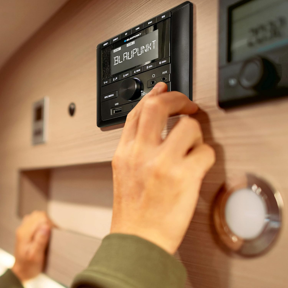 En hand justerar en bilstereo från Blaupunkt på en träpanel.