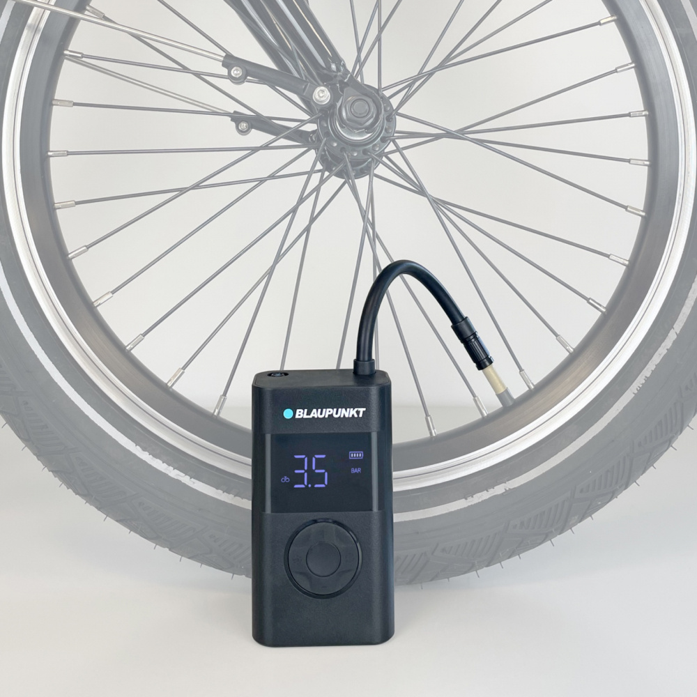 En portabel luftkompressor med digital skärm och en cykel med däck i bakgrunden.