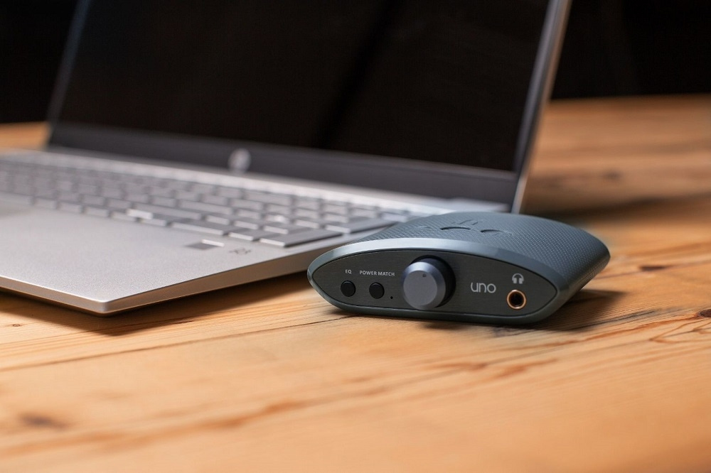 Hörlursförstärkare med USB DAC, placerad vid en laptop på ett träbord.