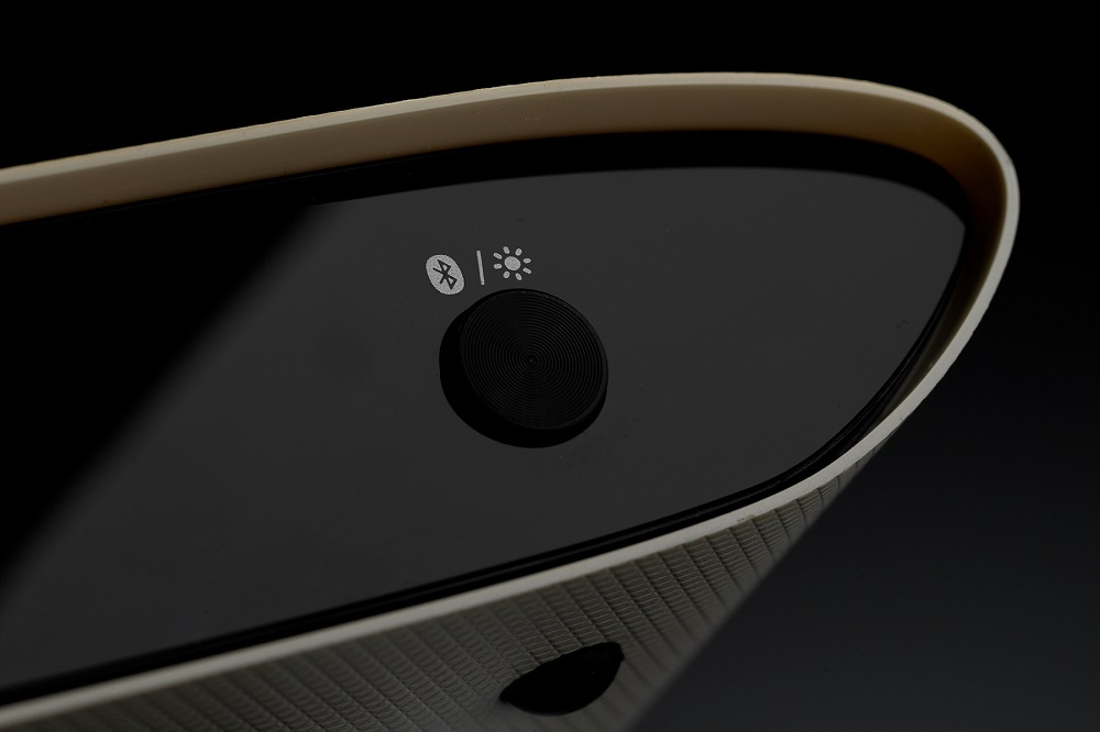 En svart yta med Bluetooth-symbol, ljusindikator och en rund knapp.