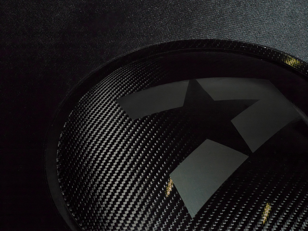Bas högtalare med kolfiberstruktur och stjärnlogotyp.