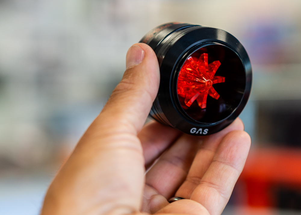 En hand håller en svart och röd diskant som ser teknologisk ut.