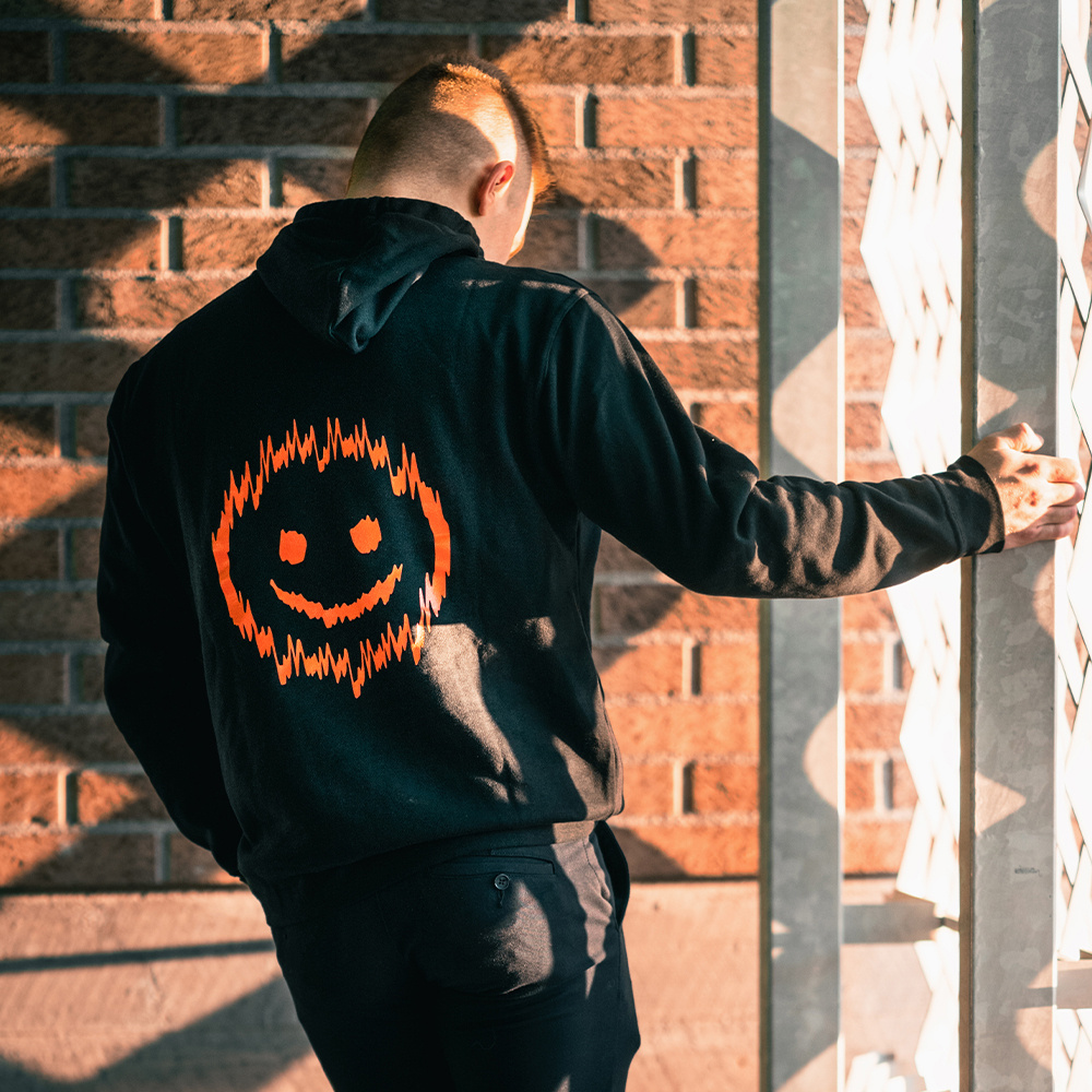 Svart hoodie med orange smiley-tryck på ryggen.