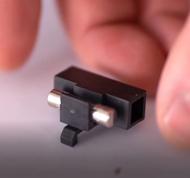 En hand håller en liten säkring med två metallkontakter.