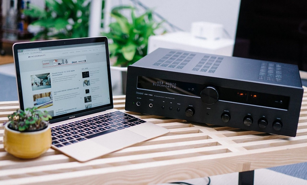 En stereoreceiver med rör bredvid en laptop på ett träbord.