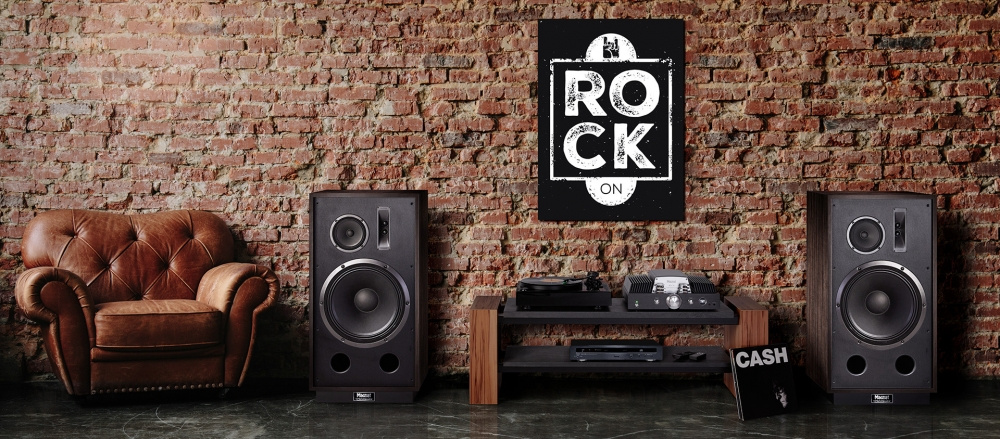 Två golvhögtalare i retrodesign i en stilren miljö med vägg av tegel.