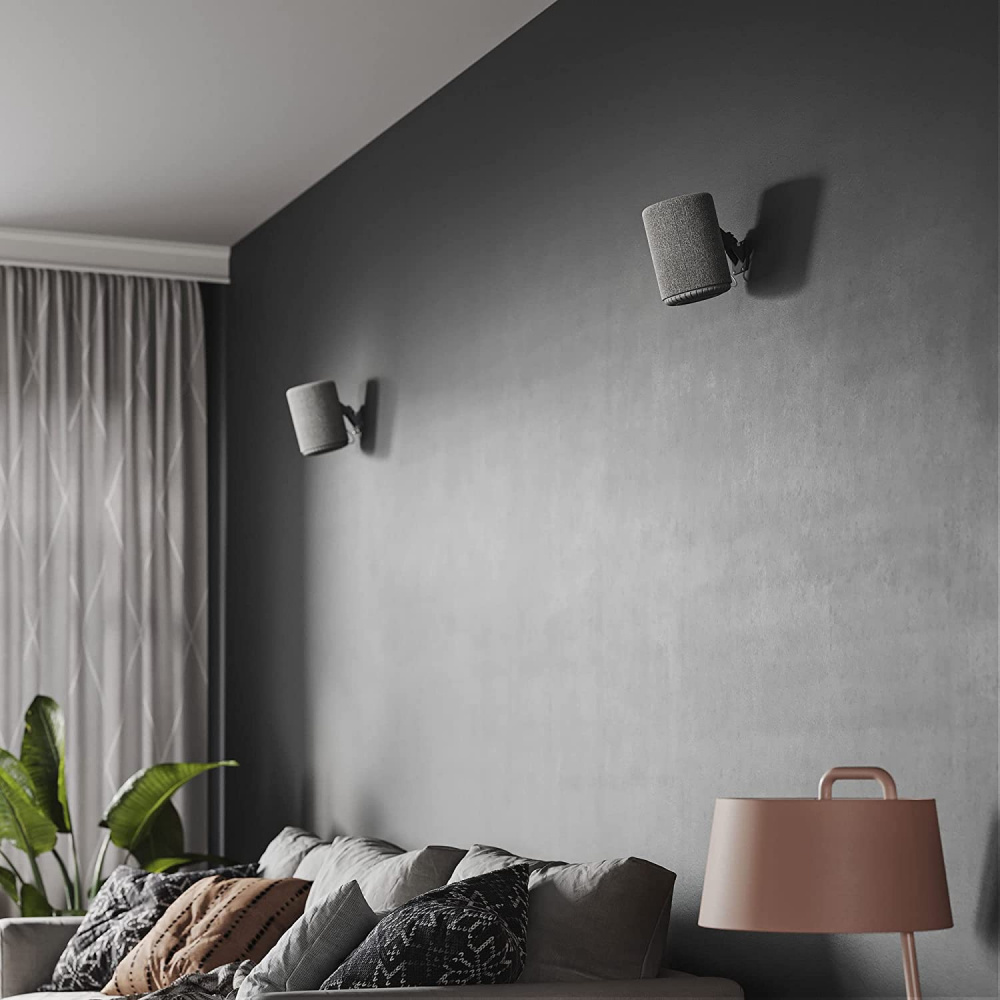 Väggmonterade högtalare ovanför en soffa i ett stilrent rum.